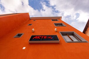 Un edificio con un cartel que dice "ARTE in HOTEL & PIZZERIA" frente a un cielo azul con nubes.