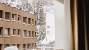 A hotel room with a view of a snow-covered building and trees. - Hotel Arte (St. Moritz)