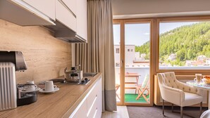 A modern kitchen with a coffee machine, a sink, and a dining area with a table and chairs. - Hotel Arte (St. Moritz)