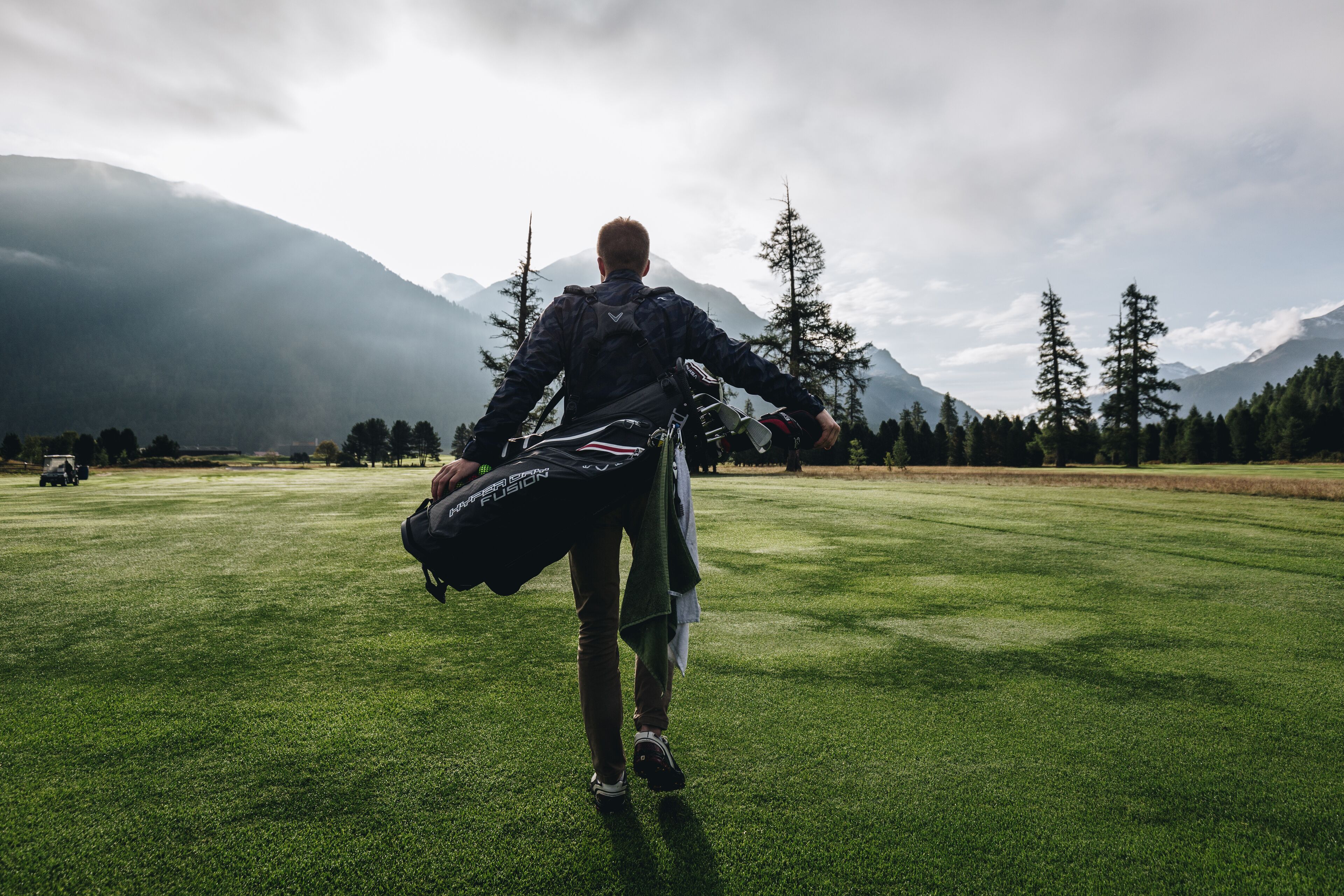 A person walking on a grassy field with mountains in the background.