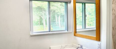 A bathroom with a white sink, a wooden-framed mirror, and a window with a view of trees.