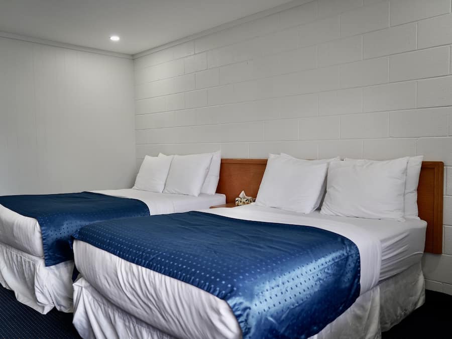 Habitación de hotel con dos camas, paredes blancas y cabecero de madera.