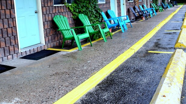 A motel with numbered doors, outdoor seating, and a parking area. - Cedar Lane Motel (Bracebridge)