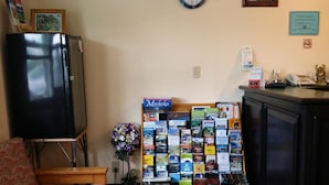 Un salon comprenant un canapé, une petite table, une horloge murale, un tableau d’affichage avec des brochures de voyage et un réfrigérateur.