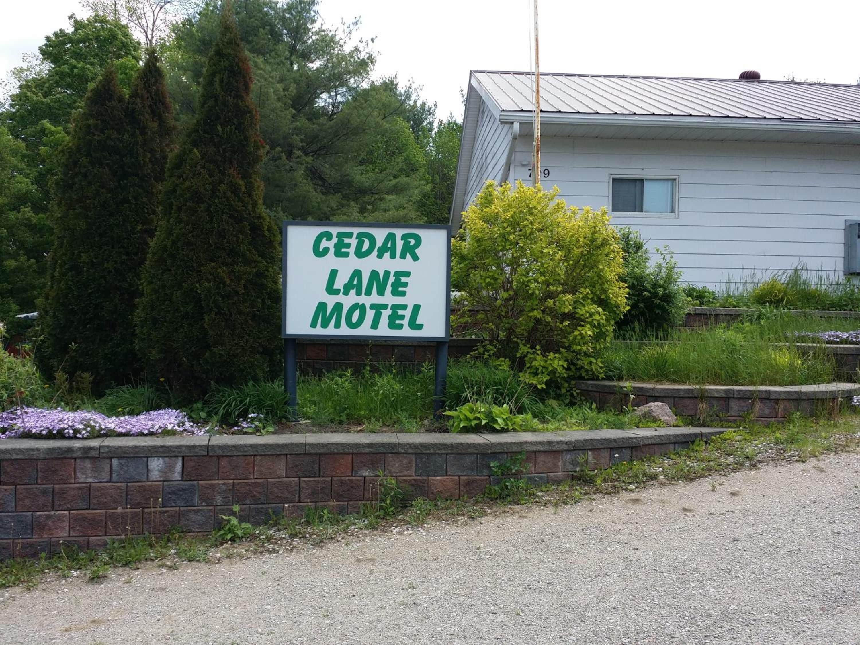 A sign for Cedar Lane Motel with a brick wall and greenery in the foreground.