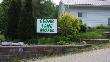 Letrero del motel Cedar Lane, con un muro de ladrillo y follaje en primer plano.