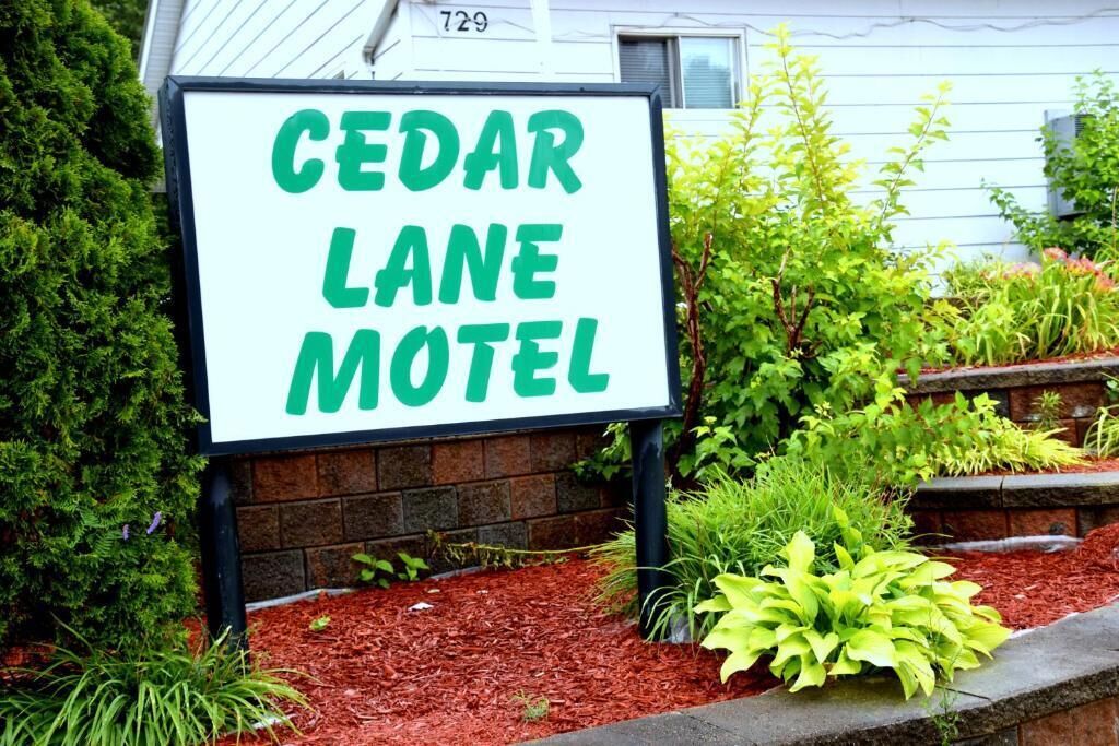 A sign for Cedar Lane Motel with a brick wall and landscaped garden in the background.