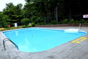 A rectangular swimming pool with a metal ladder on one side, surrounded by a brick wall and a metal fence. - Cedar Lane Motel (Bracebridge)
