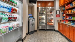 A self-service beverage station with refrigerated shelves, an ATM, and a refrigerator stocked with snacks.