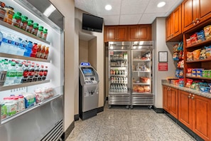 Una estación de bebidas autoservicio con estantes refrigerados, un cajero automático y un refrigerador lleno de aperitivos.