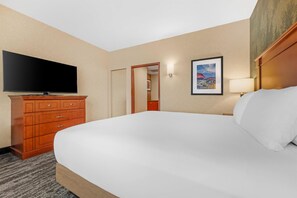 Habitación de hotel con una cama grande, una televisión de pantalla plana, un aparador de madera, un cuadro en la pared y una puerta que da a otra habitación.