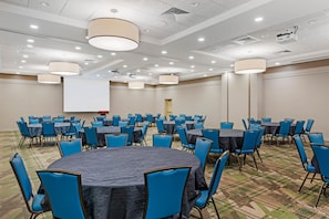 A conference room with round tables and blue chairs, equipped with a projector screen and ceiling lights. - Drury Plaza Hotel Colorado Springs Near the Air Force Academy (Colorado Springs)