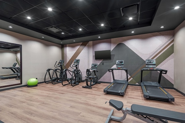 Un gimnasio con cintas de correr, elípticas, una máquina de remo, una pelota de ejercicio verde y un banco.