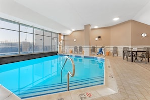 Une piscine intérieure avec des parois en verre transparent, un sol carrelé et un panneau indiquant qu’il est interdit de conduire à proximité du bord de la piscine.
