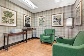 Una habitación con papel tapiz escocés, un sillón verde, un escritorio con computadora y obras de arte enmarcadas en las paredes.