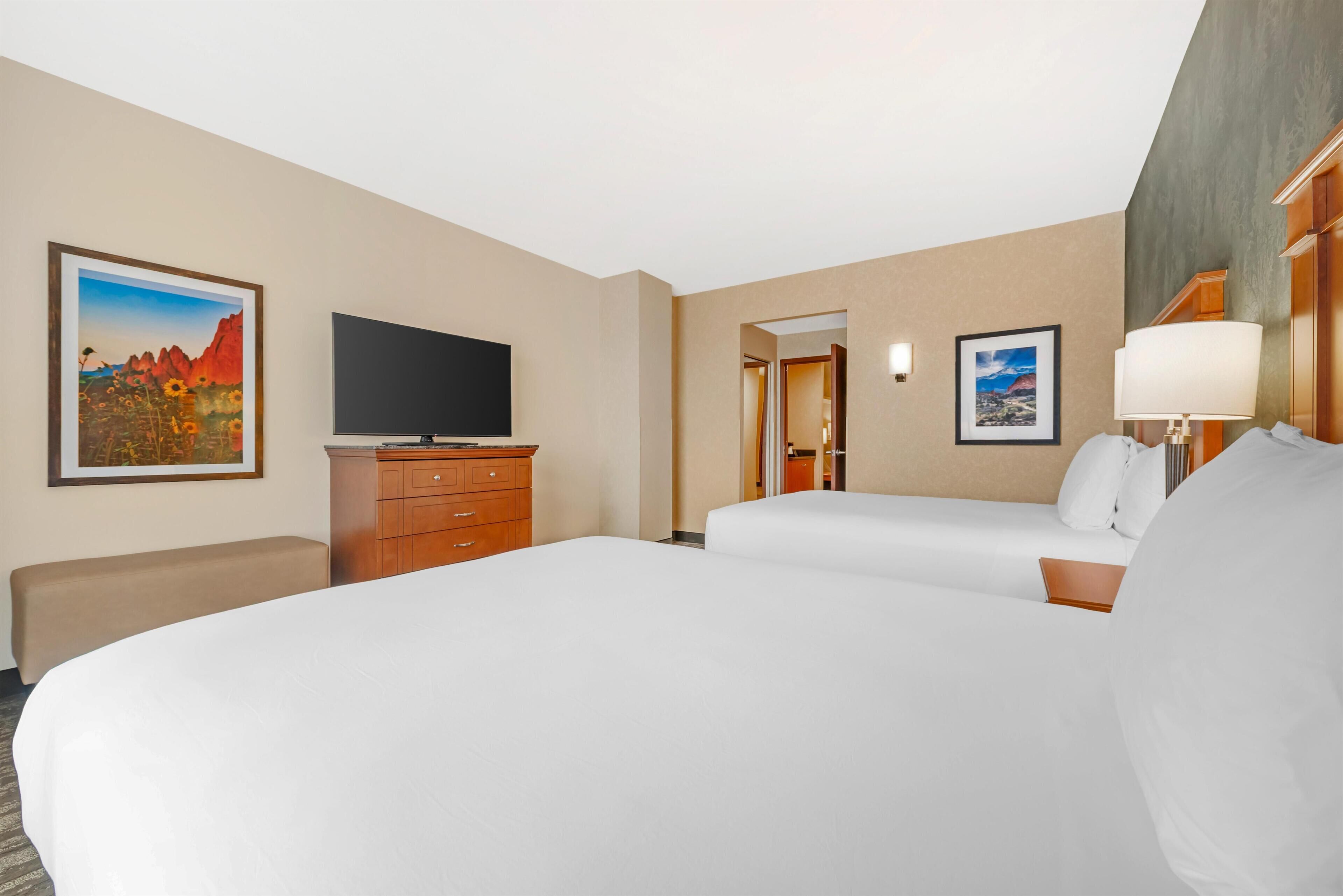 Habitación de hotel con dos camas, un televisor de pantalla plana, un aparador de madera y obras de arte en las paredes.