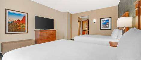 Habitación de hotel con dos camas, un televisor de pantalla plana, un aparador de madera y obras de arte en las paredes.