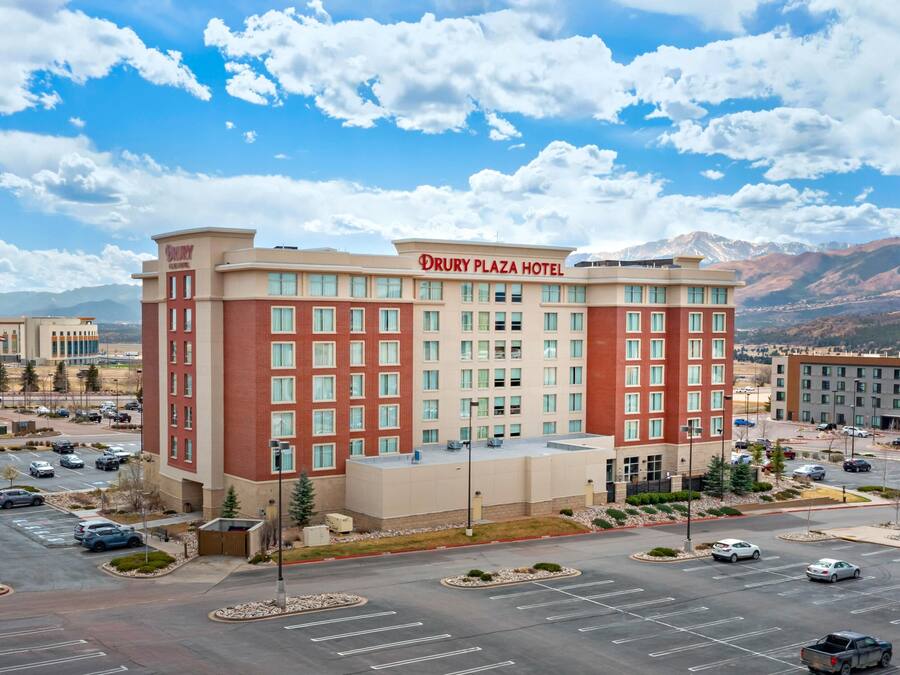 A Drury Plaza Hotel with a parking lot, a mountainous backdrop, and a clear sky.