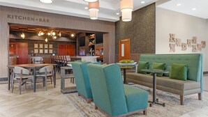 A modern hotel lobby with a kitchen bar, seating area, and a large green sofa.