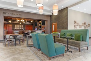 Un moderno vestíbulo de hotel con barra tipo cocina, zona de estar y un amplio sofá verde.