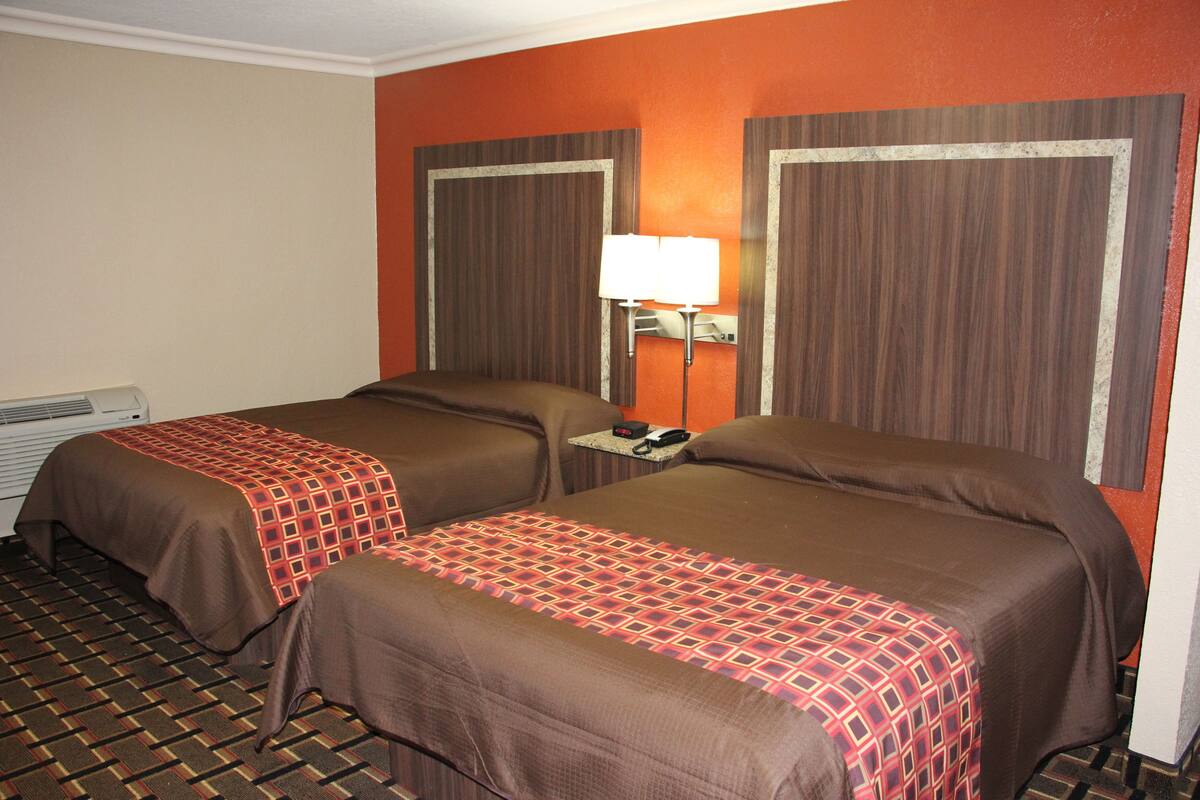 A hotel room with two beds, a heater, a nightstand with a lamp, and a telephone.