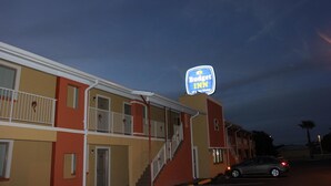 A motel with a neon sign, a staircase, and a parked car.
