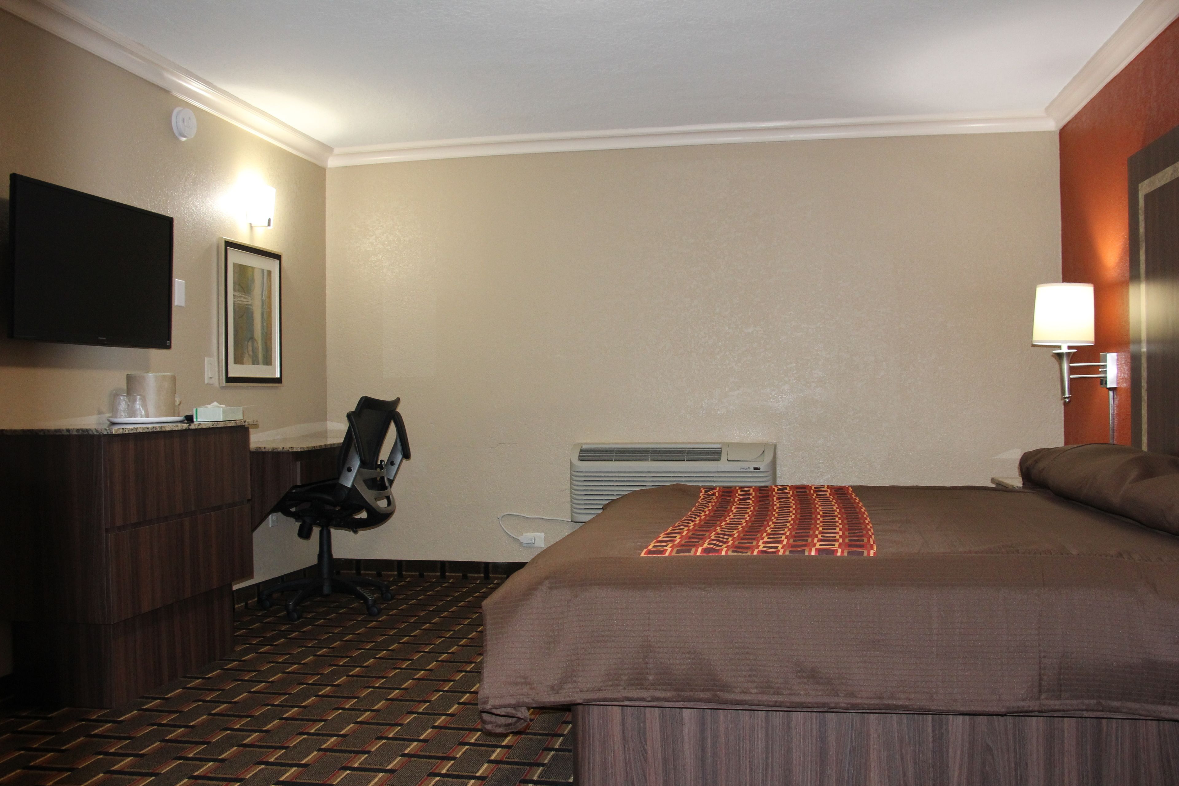 Una camera d'albergo con un letto, una scrivania con una sedia, una televisione e un condizionatore d'aria a muro.