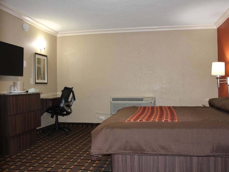 Una camera d'albergo con un letto, una scrivania con una sedia, una televisione e un condizionatore d'aria a muro.