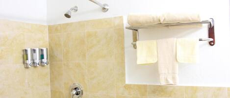 A shower area with a glass door, a towel rack with two towels, and a hand soap dispenser.