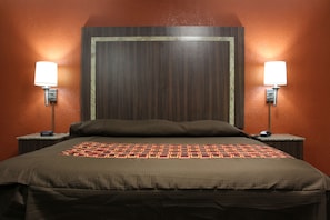 A hotel room with a large bed, two bedside tables with lamps, and a wooden headboard. - Budget Inn (Lake Wales)