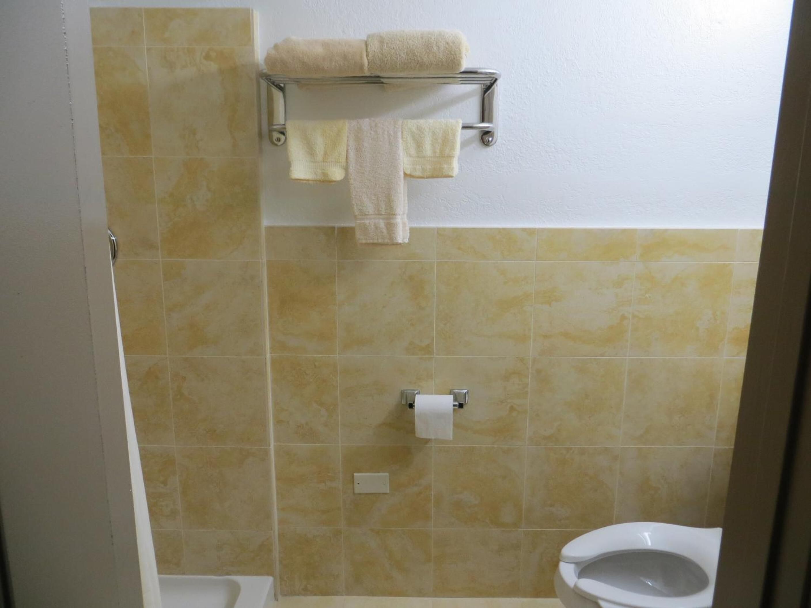 A bathroom with beige tiles, a toilet, a bidet, and a towel rack with two towels.