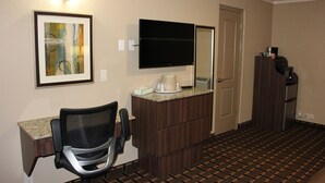 A hotel room with a desk, chair, television, and a coffee machine.
