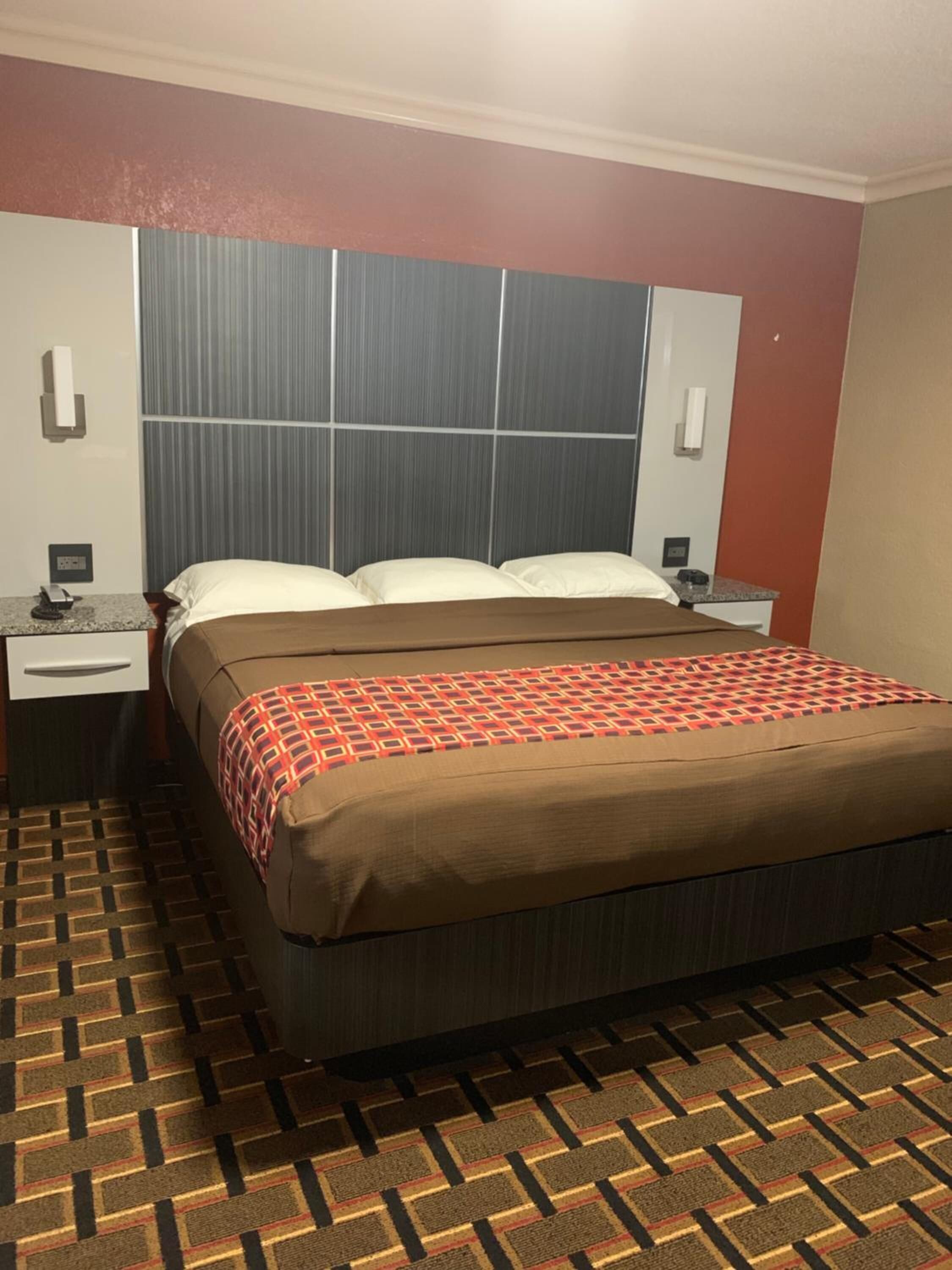 Een hotelkamer met een bed, nachtkastje en een telefoon aan de muur.