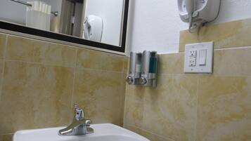 A bathroom with a sink, mirror, hand dryer, and soap dispensers.