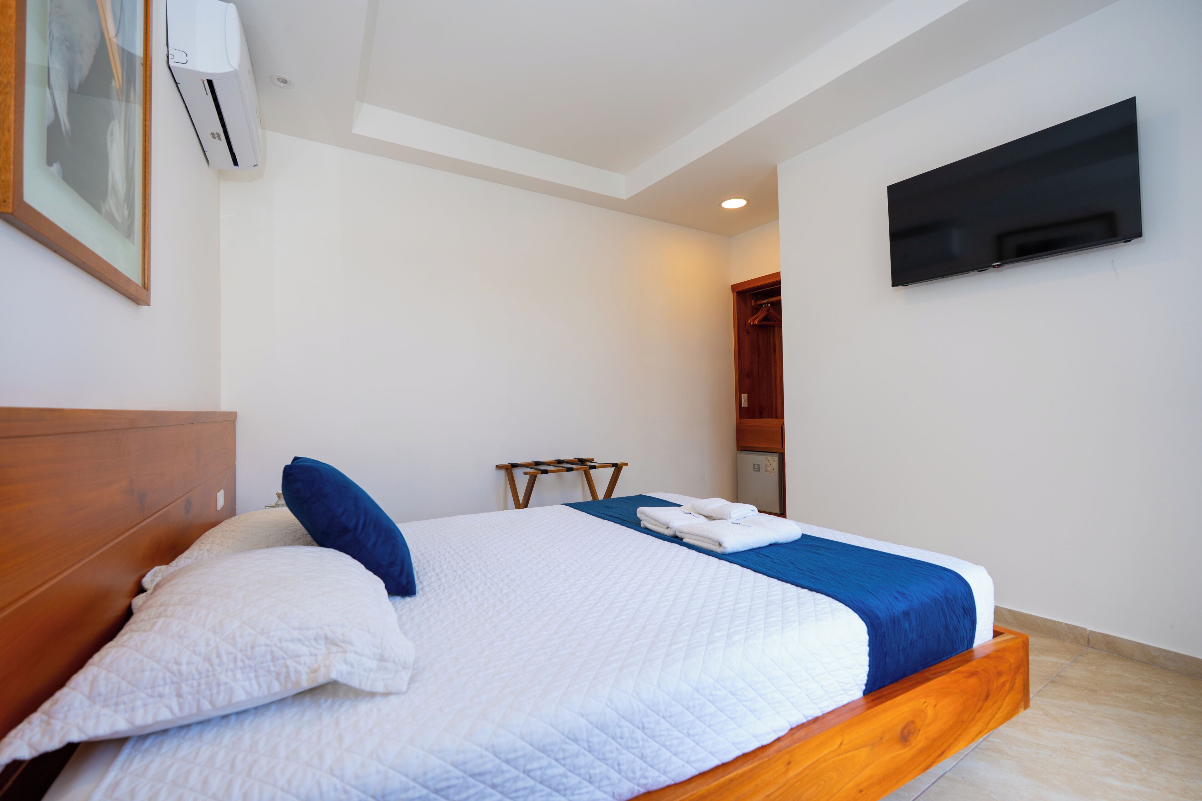 A bedroom with a bed, a TV mounted on the wall, and an air conditioning unit.