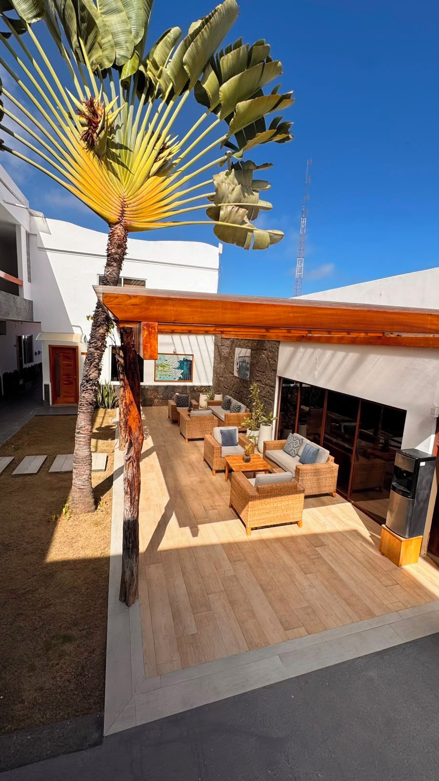 A modern outdoor living area with a wooden deck, wicker furniture, and a large fan.