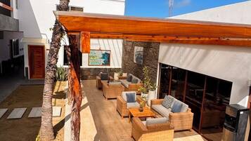 Un espacio exterior moderno con terraza de madera, mobiliario de mimbre y un ventilador grande.