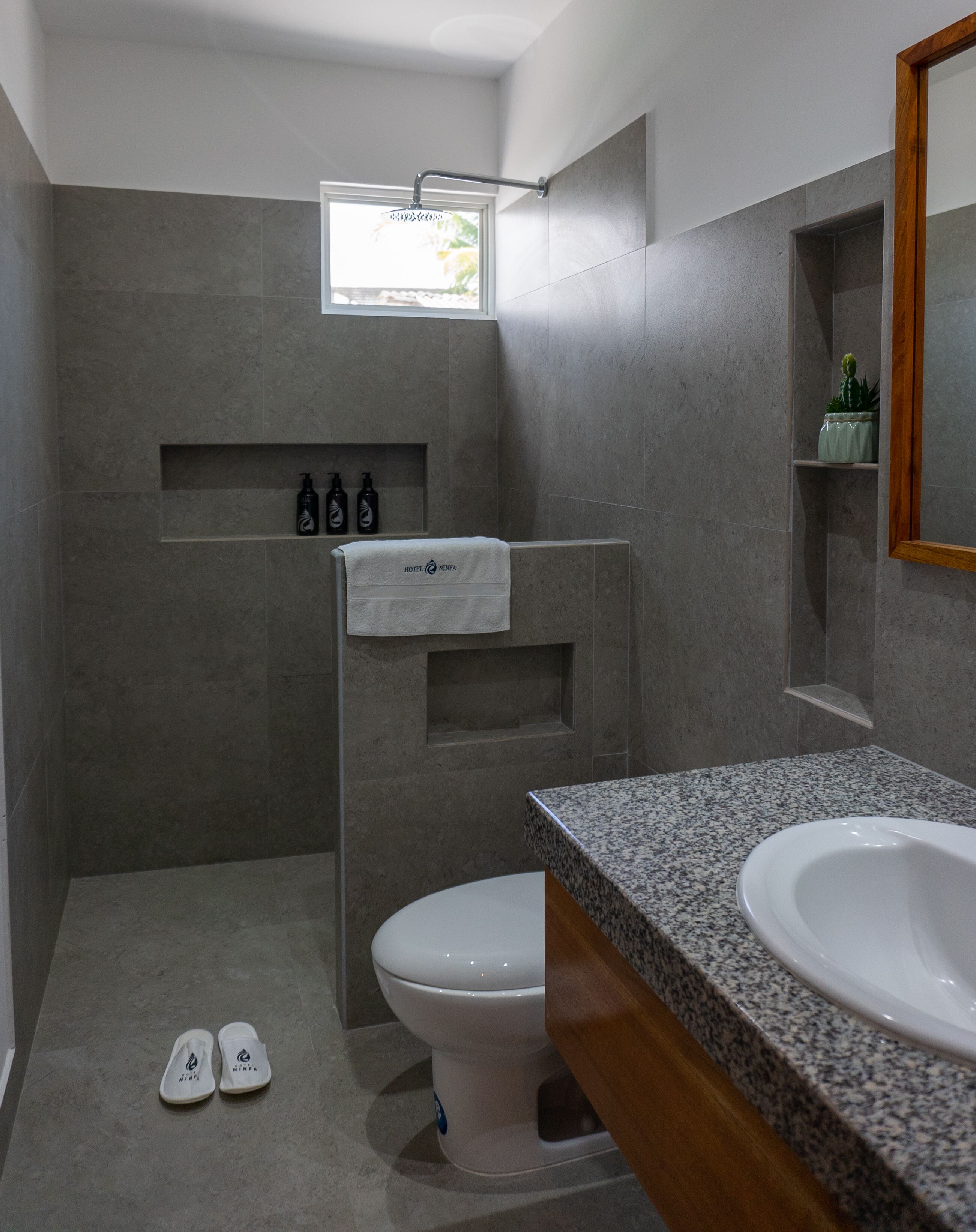 Une salle de bain moderne équipée de toilettes, d  ’un lavabo et d’une zone de douche. On trouve des articles de toilette sur une étagère et une serviette est accrochée au mur.