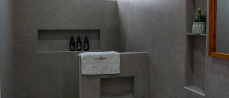 A modern bathroom with a toilet, sink, and shower area. There are toiletries on a shelf and a towel hanging on the wall.