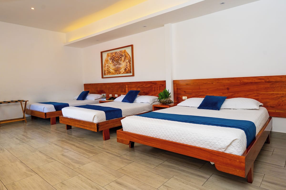 Une chambre d’hôtel avec trois lits en bois, chacun agrémenté de draps blancs et bleus.