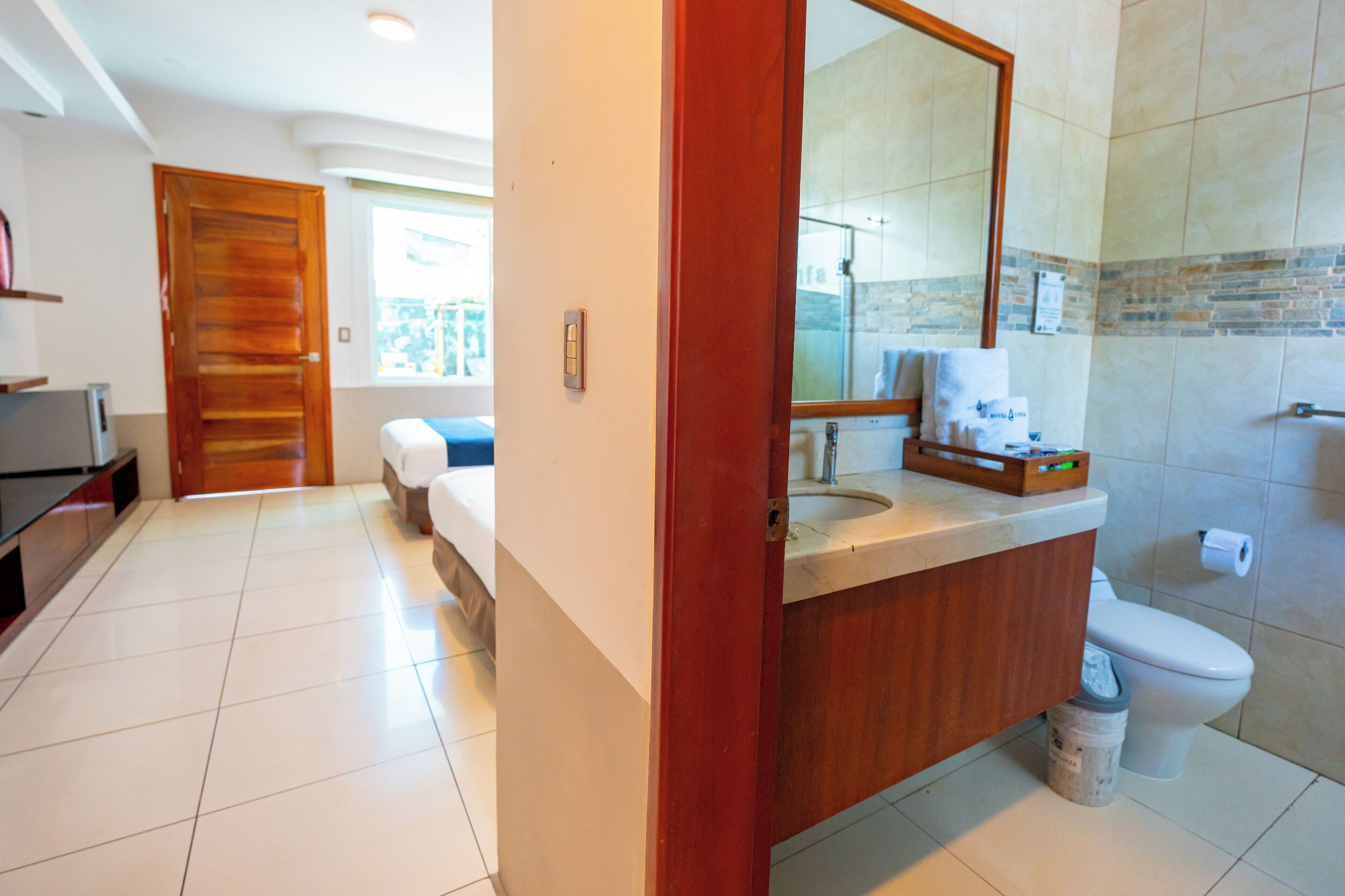 A hotel bathroom with a wooden vanity, a large mirror, a toilet, and a shower area.