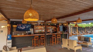 Een bar met rieten meubels, een zwembad en een televisiescherm.