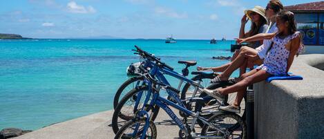 Zona costera con un área de descanso de hormigón, bicicletas y vistas al mar con barcos.