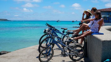 Uma área costeira com um espaço de estar de concreto, bicicletas e vista para o mar com barcos.