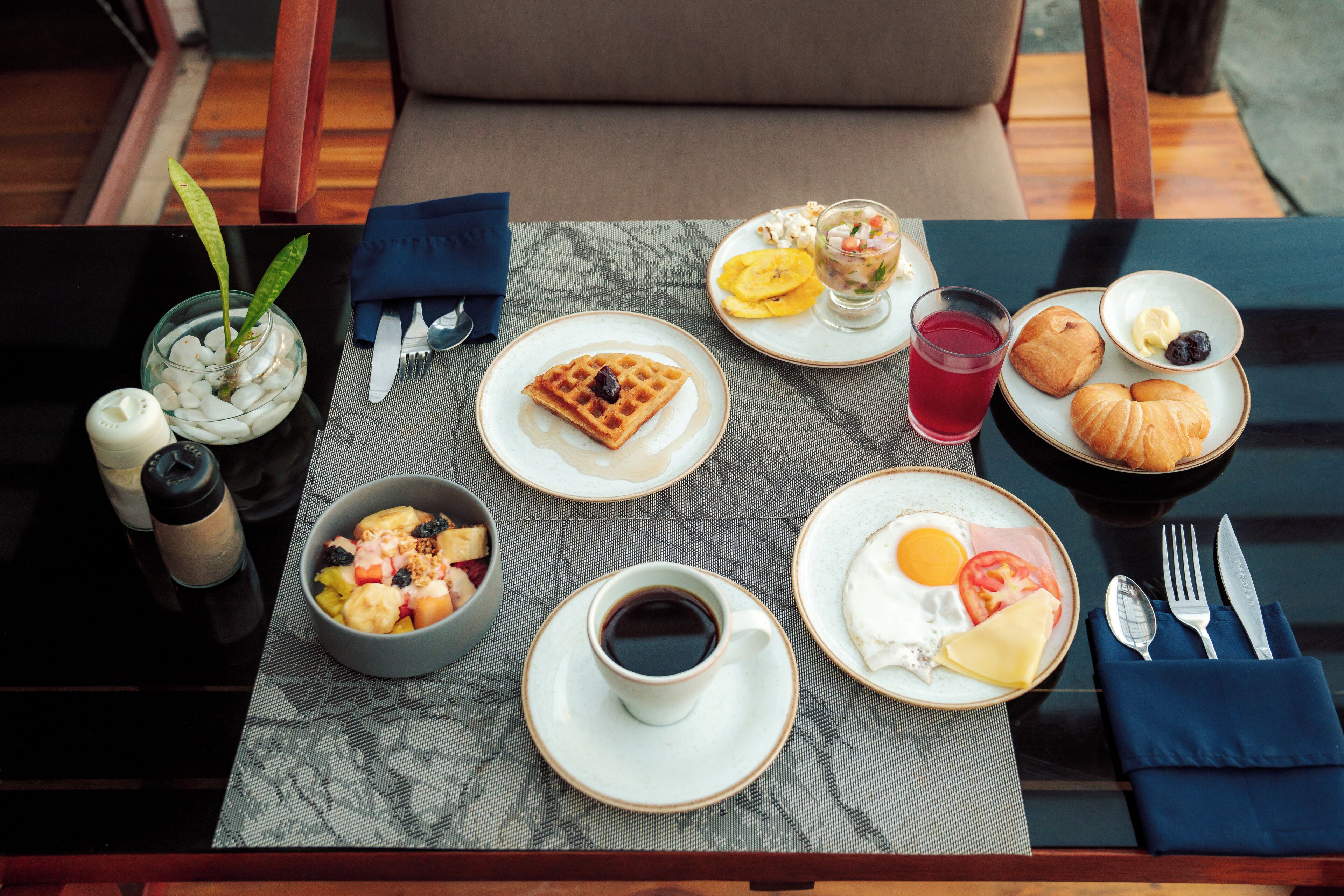 A breakfast table with a waffle, croissants, fruit, and a cup of coffee.