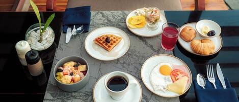 A breakfast table with a waffle, croissants, fruit, and a cup of coffee.