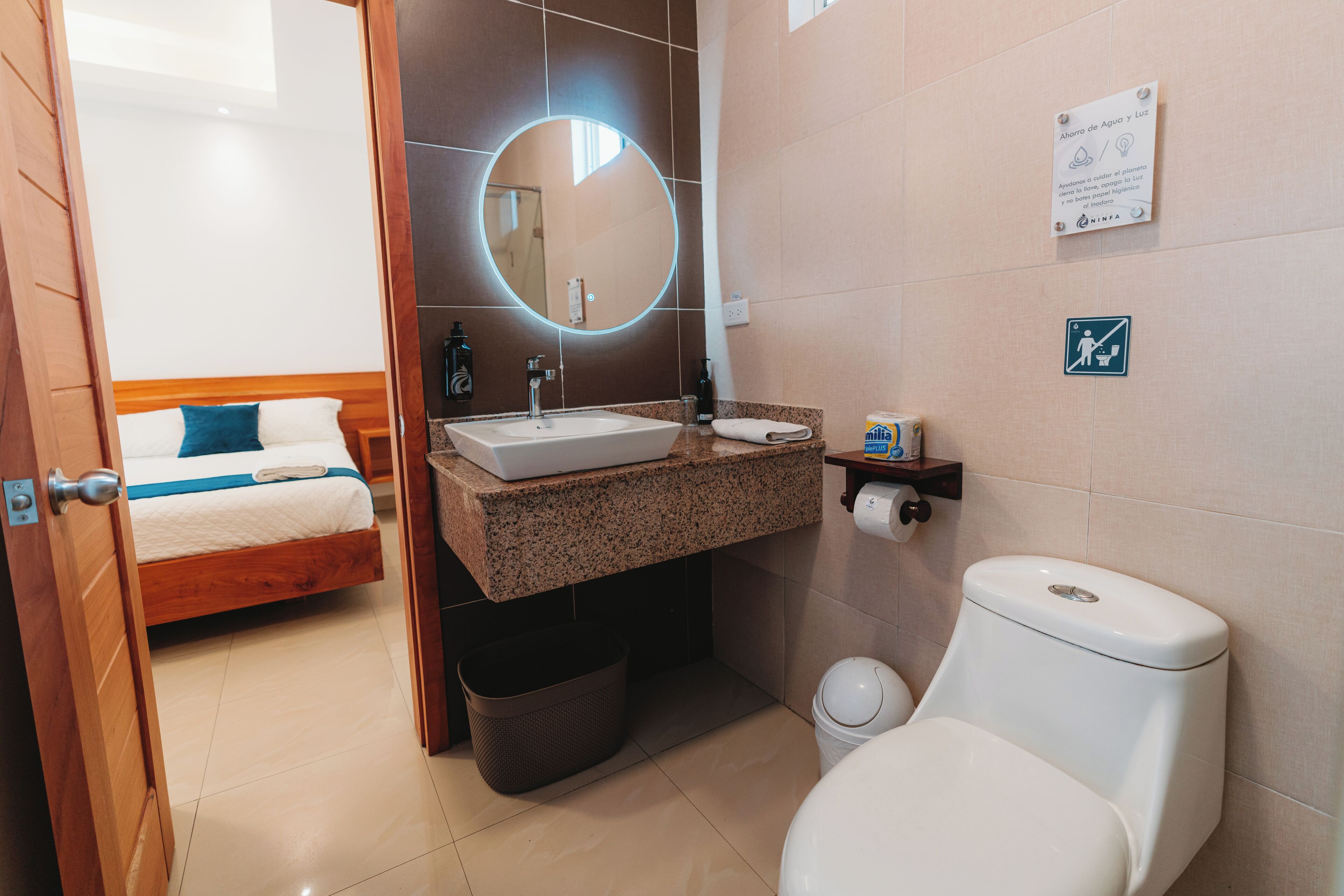 A hotel bathroom with a sink, toilet, and a mirror with a circular light.