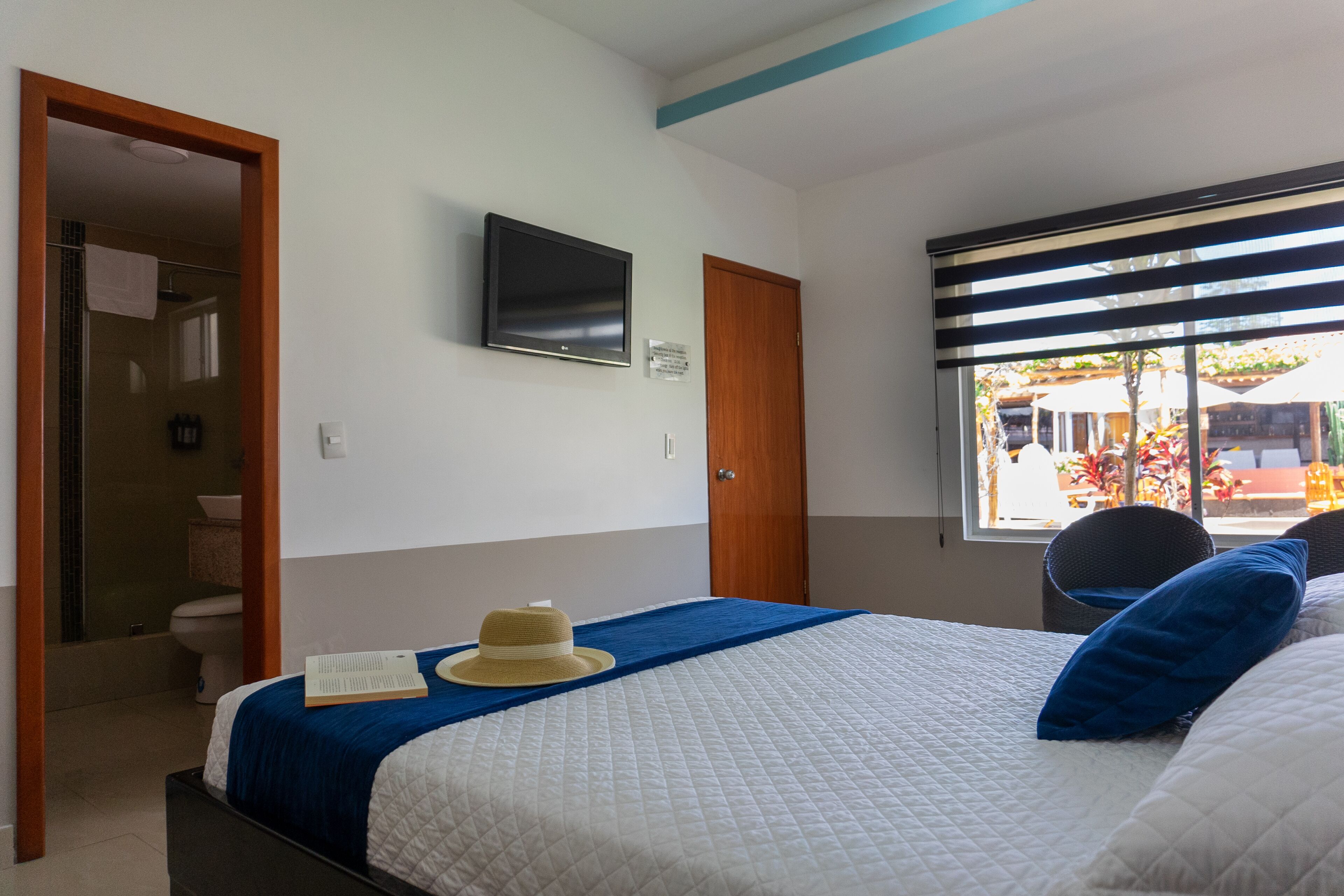 A hotel room with a bed, a television, a window with a view of the outside, and a door leading to the bathroom.