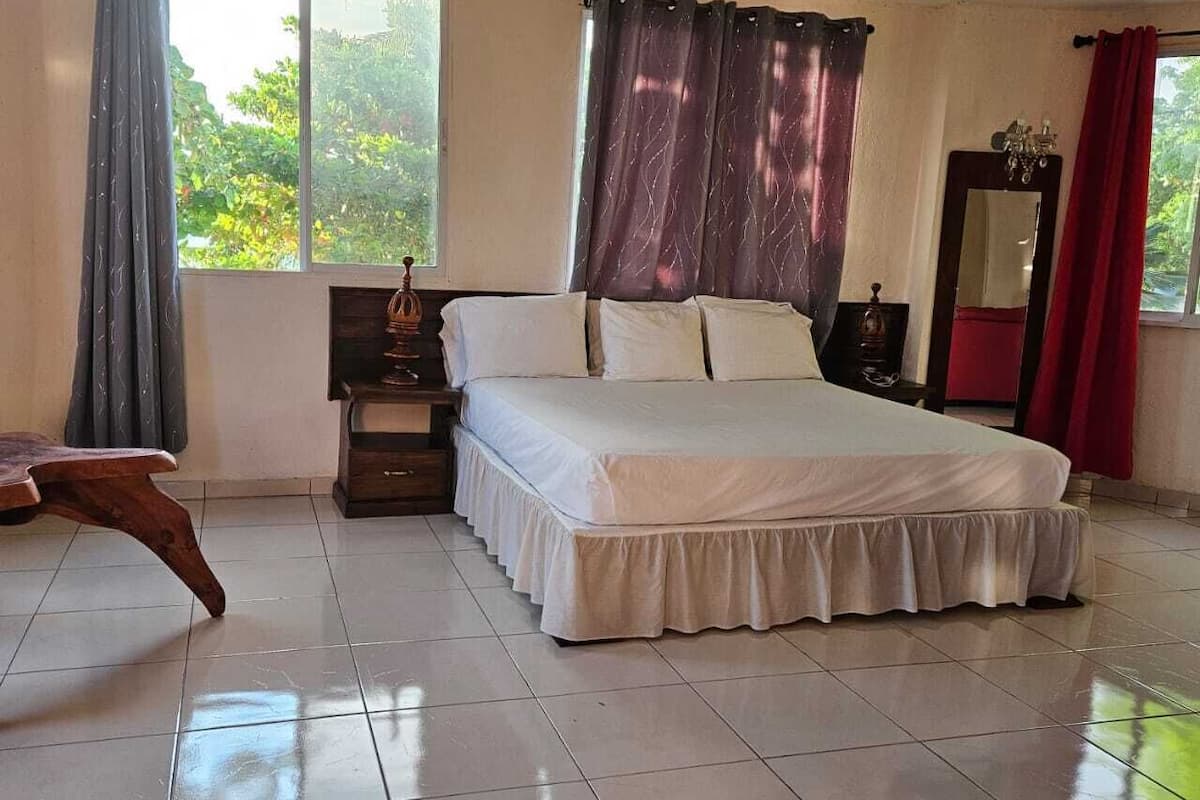 A bedroom with a large bed, a nightstand, a dresser, a mirror, and a window with curtains.