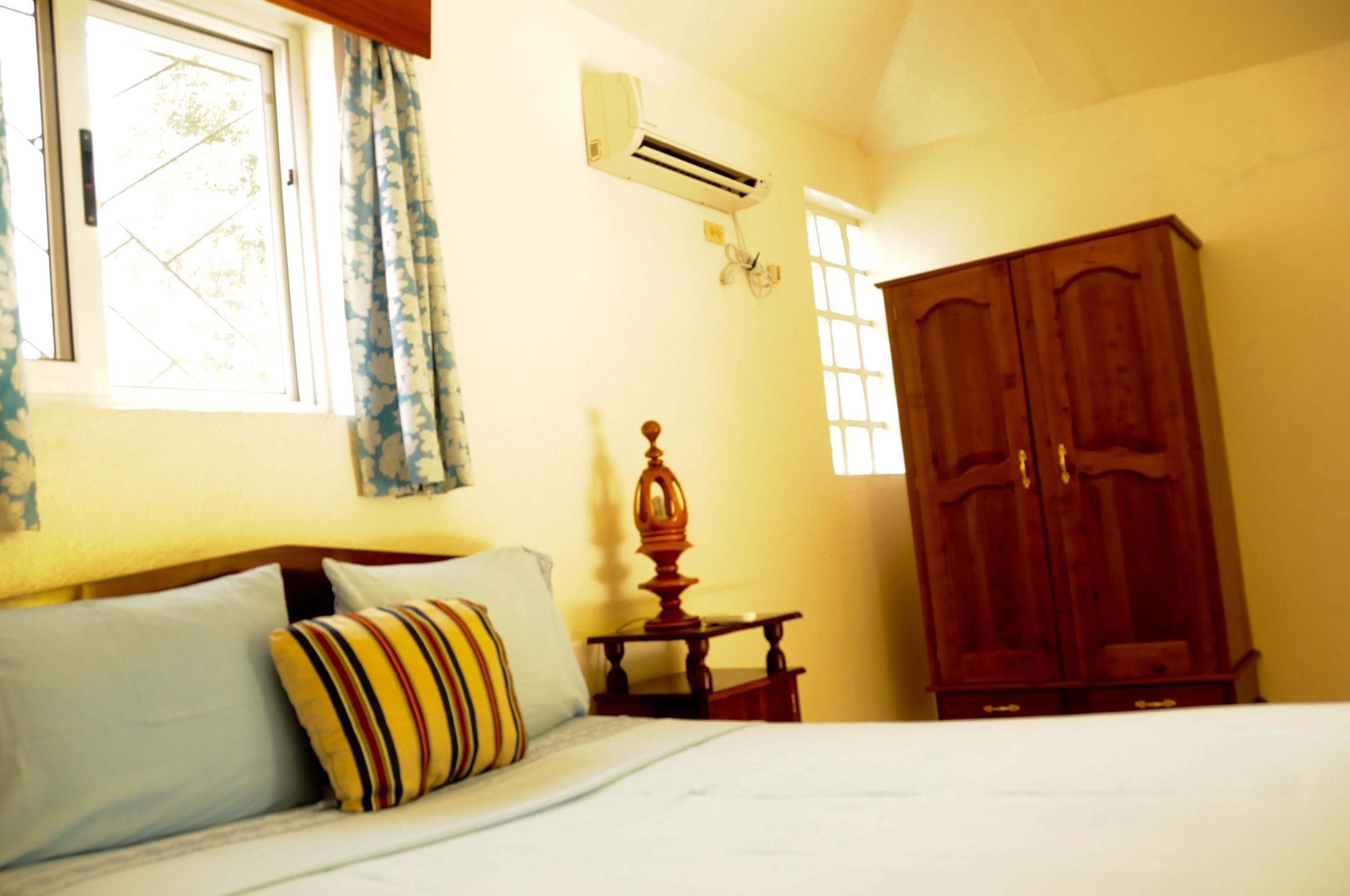 A bedroom with a bed, a wooden wardrobe, a nightstand, and an air conditioning unit.
